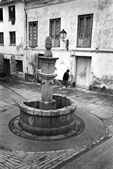 A woman walks past an old stone drinking water fountain A woman walks past an old stone drinking water fountain
