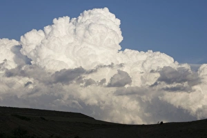 Low altitude billowing cumulus clouds on horizon looming above dark foreground Low altitude billowing cumulus clouds on horizon looming above dark foreground