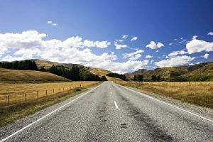Road - long straight deserted tarmac paved road, rolling hills, white clouds, blue sky Road - long straight deserted tarmac paved road, rolling hills, white clouds, blue sky