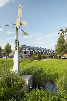 Prints of Small windmill used to drive a pump, which alters water levels in irrigation ditches. Behind the windmill are a row of houses (centre) that have solar panels fitted into the roofline Images Dated 2008 August: Small Windmill Print