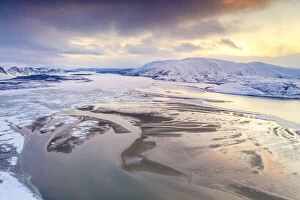 Aerial view of cold sea framed by snow capped mountains at sunset