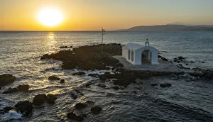 Aerial view of the small church of Agios Nikolaos on islet by the rough sea at sunrise, Georgioupolis, Crete island Aerial view of the small church of Agios Nikolaos on islet by the rough sea at sunrise, Georgioupolis, Crete island