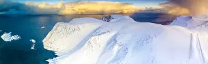Aerial view of sunrise on snow capped mountains and blue arctic sea, Sorvaer