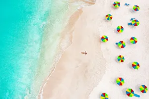 Aerial view of woman in bikini sunbathing on a tropical beach next to colorful umbrellas, Antigua, West Indies Aerial view of woman in bikini sunbathing on a tropical beach next to colorful umbrellas, Antigua, West Indies