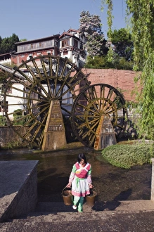 A Bai girl carrying buckets of water in front of a water wheel in Lijiang Old Town A Bai girl carrying buckets of water in front of a water wheel in Lijiang Old Town