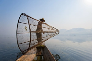 A basket fisherman on Inle Lake prepares to plunge his cone shaped net, Shan State A basket fisherman on Inle Lake prepares to plunge his cone shaped net, Shan State