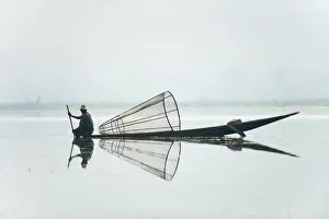 A basket fisherman on Inle Lake scans the still and shallow water for signs of life