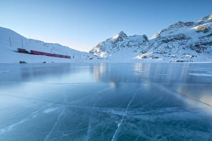 The Bernina Express train runs beside the frozen Lago Bianco, Bernina Pass, canton of Graubunden The Bernina Express train runs beside the frozen Lago Bianco, Bernina Pass, canton of Graubunden