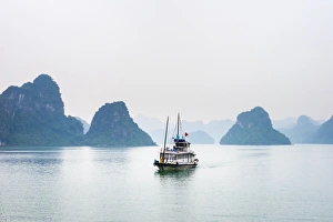 A boat passes through foggy karst landscape in Ha Long Bay, Quang Ninh Province, Vietnam A boat passes through foggy karst landscape in Ha Long Bay, Quang Ninh Province, Vietnam
