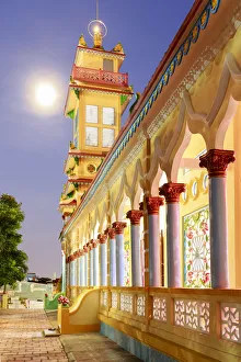 The Cao Dai temple in Vung Tau lit up at dusk with the full moon to the left of the tower The Cao Dai temple in Vung Tau lit up at dusk with the full moon to the left of the tower