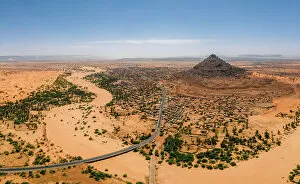 Riverbed Gallery: A crumbling mountain, a river bed, palms, and dunes surround the village of Kamour, Mauritania