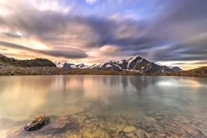 Dramatic sky at sunrise over Tresero peak reflected in lake Manzina, Valfurva, Valtellina Dramatic sky at sunrise over Tresero peak reflected in lake Manzina, Valfurva, Valtellina