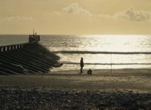 Fisherman on the beach silhouetted against the winter sun where the Arun estuary enters the sea