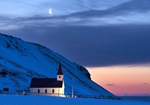 Floodlit church at dawn against snow covered mountains, winter, near Vik, South Iceland Floodlit church at dawn against snow covered mountains, winter, near Vik, South Iceland