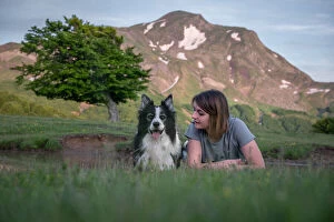 A girl and her border collie dog lying in the grass with a tree and mountain in the background, Emilia Romagna, Italy