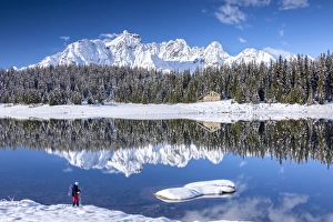 Hiker admires the snowy peaks and woods reflected in Lake Palu, Malenco Valley, Valtellina Hiker admires the snowy peaks and woods reflected in Lake Palu, Malenco Valley, Valtellina
