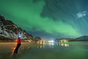 Hiker with head torch watching the Aurora Borealis (Northern Lights) standing on Ramberg beach, Nordland county, Lofoten Islands, Norway, Scandinavia, Europe