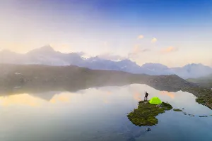 Hiker man with tent admiring a misty sunrise over mountains from Obere Schwarziseeli lake Hiker man with tent admiring a misty sunrise over mountains from Obere Schwarziseeli lake