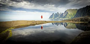 Hiker man walking on water's edge admiring mountains reflected in the sea, Tungeneset Hiker man walking on water's edge admiring mountains reflected in the sea, Tungeneset