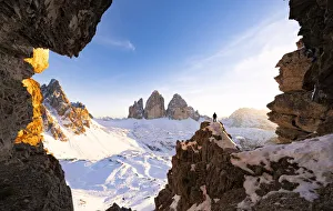 Hiker on rocks admiring Tre Cime di Lavaredo and Monte Paterno covered with snow at Hiker on rocks admiring Tre Cime di Lavaredo and Monte Paterno covered with snow at