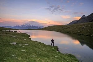 Images Dated 28th July 2013: Hiker on the shore admires the pink colors of dawn reflected in Lake Campagneda, Malenco Valley