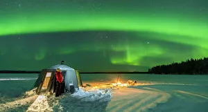Hiker watching the Aurora Borealis (Northern Lights) close to bonfire and igloo in the frozen landscape, Jokkmokk Hiker watching the Aurora Borealis (Northern Lights) close to bonfire and igloo in the frozen landscape, Jokkmokk