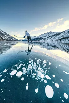 Ice hockey player skating on frozen Lake Sils covered of bubbles, Engadine