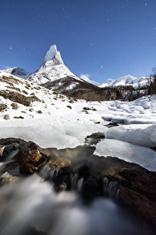Ice on rocks frames the granitic snowy peak of the Stetind mountain under the starry sky Ice on rocks frames the granitic snowy peak of the Stetind mountain under the starry sky