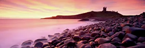 An imposing silhouette of Dunstanburgh Castle against a magnificent sky at sunrise with a An imposing silhouette of Dunstanburgh Castle against a magnificent sky at sunrise with a