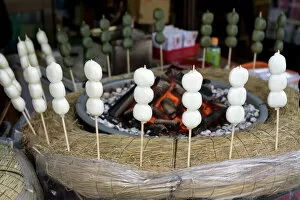 Japanese snack called dango (three sticky rice cake balls on a skewer) warming beside hot coals