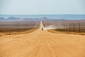 A jeep on a long sandy road in southern Namibia leaves a trail of dust, Namibia, Africa A jeep on a long sandy road in southern Namibia leaves a trail of dust, Namibia, Africa