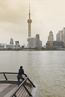 A man looking at the Oriental Pearl Tower and Pudong skyline across the Huangpu River A man looking at the Oriental Pearl Tower and Pudong skyline across the Huangpu River