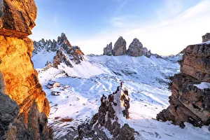 Man on rocks admiring the snowy Monte Paterno and Tre Cime di Lavaredo at sunset Man on rocks admiring the snowy Monte Paterno and Tre Cime di Lavaredo at sunset