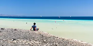Man sitting on rocks looking at the kitesurfers in the clear sea, Sotavento beach, Jandia Man sitting on rocks looking at the kitesurfers in the clear sea, Sotavento beach, Jandia