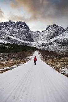 Man walking on empty mountain road covered with snow in winter, Nusfjord, Nordland county, Lofoten Islands, Norway Man walking on empty mountain road covered with snow in winter, Nusfjord, Nordland county, Lofoten Islands, Norway