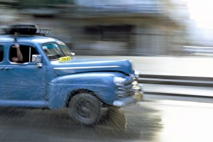 Panned shot of old American car splashing through puddle on Prado, Havana Panned shot of old American car splashing through puddle on Prado, Havana