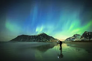 Person photographing the bright sky during Aurora Borealis (Northern Lights) standing on Skagsanden beach Person photographing the bright sky during Aurora Borealis (Northern Lights) standing on Skagsanden beach