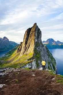 Person standing in front of tall Segla Mountain and fjords at dawn, Senja island Person standing in front of tall Segla Mountain and fjords at dawn, Senja island