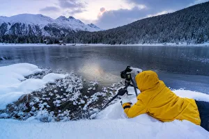 Photographer taking pictures of frozen Lej da Staz at dawn lying on the snow, Engadine Photographer taking pictures of frozen Lej da Staz at dawn lying on the snow, Engadine