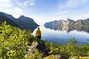 Rear view of photographer admiring the Mefjord blue water standing on rocks, Senja Rear view of photographer admiring the Mefjord blue water standing on rocks, Senja