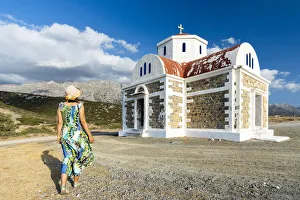 Rear view of woman in dress and straw hat walking to the Greek Orthodox church of Agia Rear view of woman in dress and straw hat walking to the Greek Orthodox church of Agia
