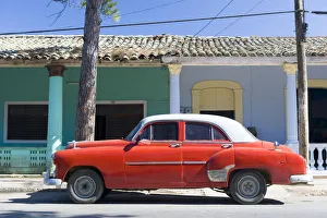 Red vintage American car parked on street next to colourful buildings in Vinales Red vintage American car parked on street next to colourful buildings in Vinales