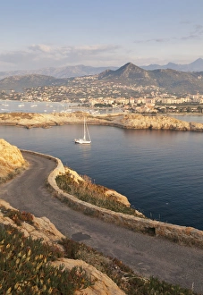 A sail boat in the clear sea around the village of Ile Rousse at sunset, Balagne Region A sail boat in the clear sea around the village of Ile Rousse at sunset, Balagne Region