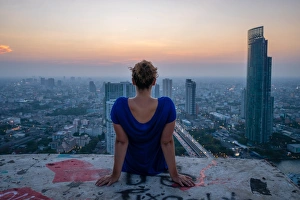A single woman watching sun set over city skyline at dusk, Bangkok, Thailand A single woman watching sun set over city skyline at dusk, Bangkok, Thailand