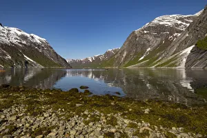 Snow capped mountains reflected in the still waters of the fjord where kayakers are Snow capped mountains reflected in the still waters of the fjord where kayakers are