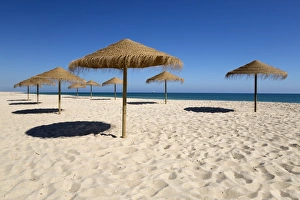 Straw umbrellas on empty white sand beach with clear sea behind, Ilha do Farol, Culatra Straw umbrellas on empty white sand beach with clear sea behind, Ilha do Farol, Culatra