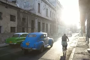 Images Dated 29th March 2011: Street scene bathed in early morning sunlight showing old American cars and cyclists