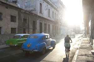 Images Dated 29th March 2011: Street scene bathed in early morning sunlight showing old American cars and cyclists