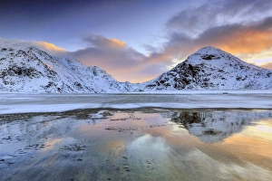 Sunrise on Uttakleiv beach surrounded by snow covered mountains reflected in the cold sea Sunrise on Uttakleiv beach surrounded by snow covered mountains reflected in the cold sea