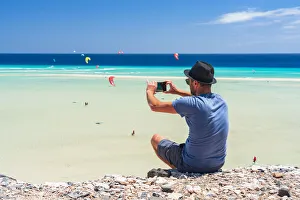 Tourist with straw hat photographing kiteboarders with smartphone at Sotavento beach Tourist with straw hat photographing kiteboarders with smartphone at Sotavento beach